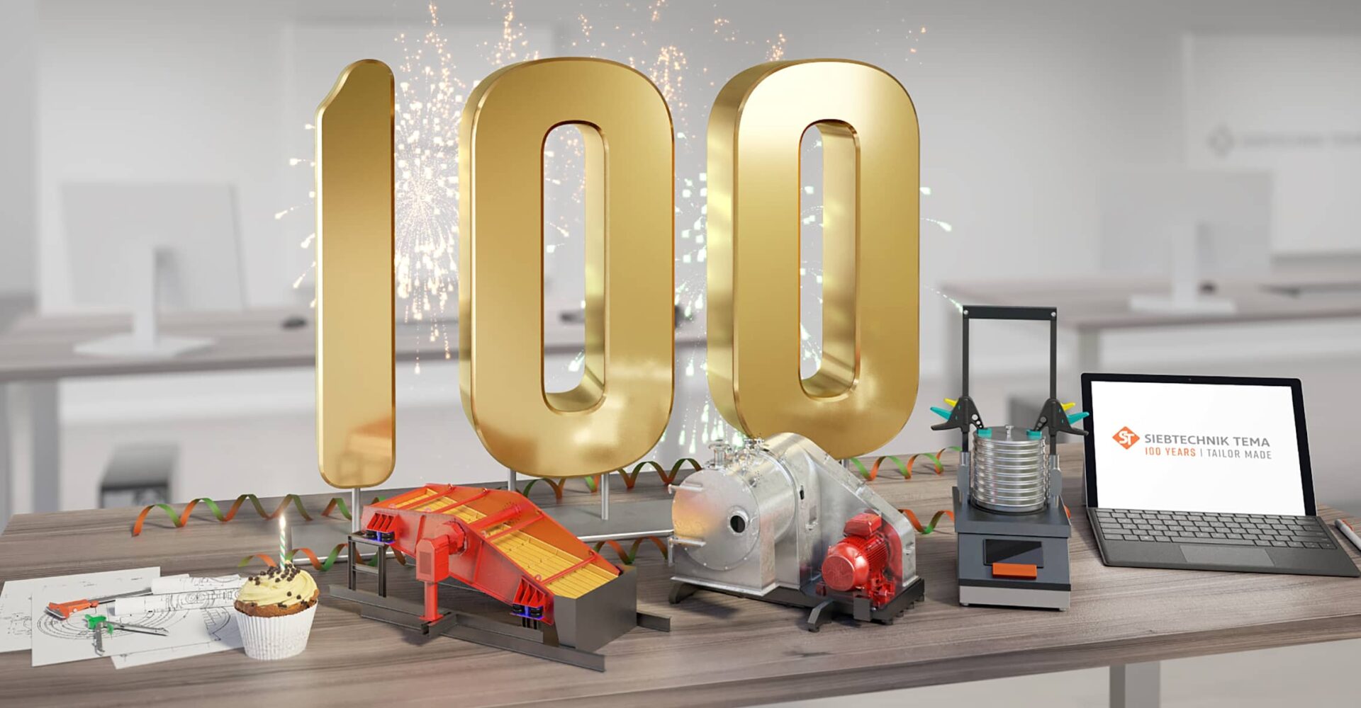 100 years SIEBTECHNIK TEMA, office with a desk on which a big golden 100 is standing, in front of it are models of some machines, a construction sketch and a laptop. The machines are a centrifuge, a screening machine and a test sieve shaker.